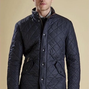 May include: Navy blue quilted jacket with a diamond pattern, featuring a brown collar and trim. The jacket has a button-up front, two front pockets, and a zipper. A classic outerwear piece.