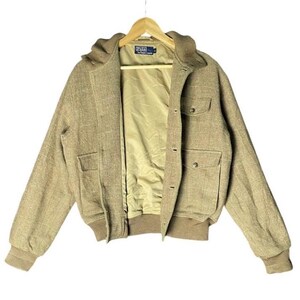 May include: A tan bomber jacket with a hood, two front pockets, and button closures. The jacket has a light brown lining and ribbed cuffs and hem. The Polo by Ralph Lauren logo is visible on the label.