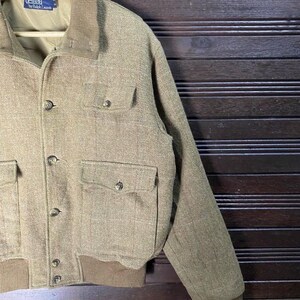 May include: A tan Polo by Ralph Lauren jacket with a corduroy collar and four front pockets. The jacket has a button-up closure and ribbed cuffs and hem. The jacket is hanging on a wooden hanger.