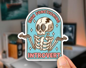 May include: A die-cut sticker featuring a cartoon skeleton with a shrug gesture against a light blue background. The text reads HIGH FUNCTIONING at the top and INTROVERT at the bottom in pink letters. Small white stars are scattered around the skeleton.