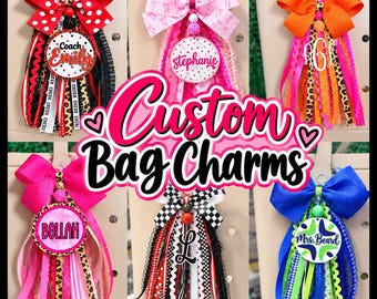 May include: Six custom bag charms featuring large fabric bows, beaded accents, and circular personalized tags with names like Coach Emily, Stephanie, Bellah, and Mrs. Beard, hanging from ribbons in various colors, patterns, and textures.