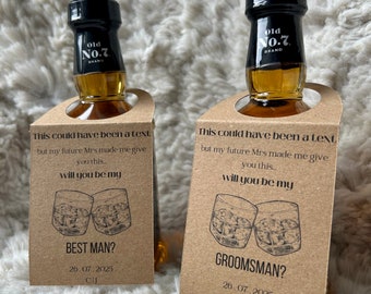 May include: Two miniature liquor bottles with brown paper tags. The tags have a black and white illustration of two glasses of liquor and the text "This could have been a text but my future Mrs made me give you this... will you be my BEST MAN? 26.07.2025 CIJ" and "This could have been a text but my future Mrs made me give you this... will you be my GROOMSMAN? 26.07.2025 CIJ".