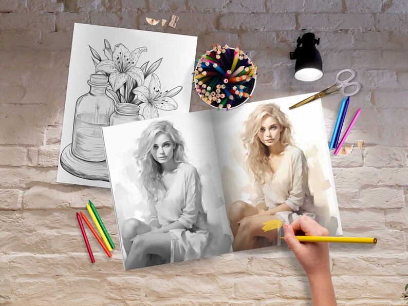 May include: An open coloring book with a black and white illustration of a woman on the left page and a colored illustration of a woman on the right page. The book is on a brick wall surface with colored pencils, a pencil sharpener, and a lamp.