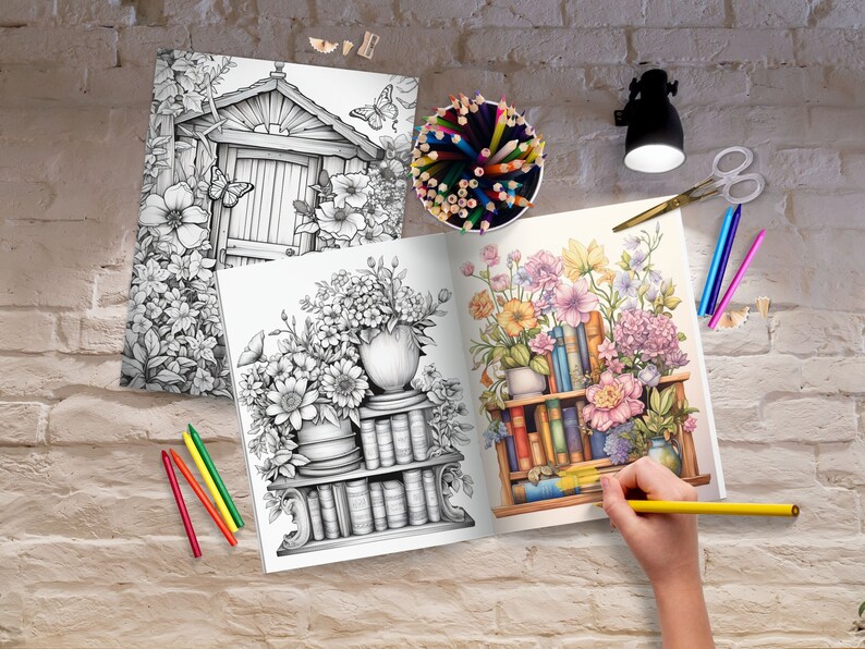 May include: An open coloring book with two pages showing detailed black and white illustrations of flowers and bookshelves. A hand is holding a yellow pencil over the open book.