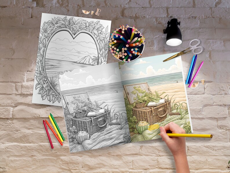 Op de afbeelding: Een open kleurboek met een zwart-witte illustratie van een picknickmand op een strand. Het boek is open op een pagina met een gekleurde illustratie van dezelfde sc&egrave;ne. Een hand houdt een geel potlood vast en kleurt de illustratie.