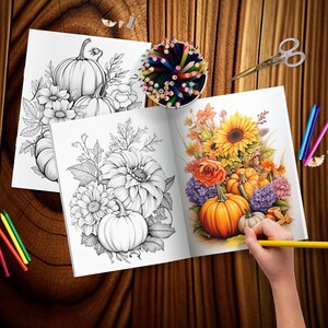 May include: An open coloring book with two pages showing black and white illustrations of pumpkins and flowers. The left page shows a group of pumpkins with leaves and flowers. The right page shows a bouquet of sunflowers, roses, and other flowers with pumpkins at the bottom. A hand is holding a yellow colored pencil over the open book.
