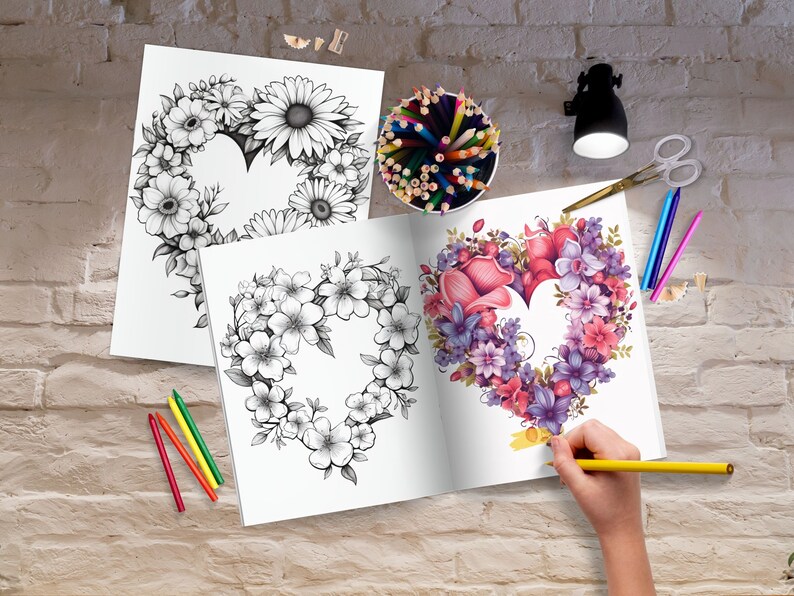 K&ouml;nnte beinhalten: Ein offenes Malbuch mit zwei Seiten, die ein herzf&ouml;rmiges Blumenmuster zeigen. Eine Seite ist mit rosa, lila und roten Blumen gef&auml;rbt, w&auml;hrend die andere Seite schwarzwei&szlig; ist. Eine Hand h&auml;lt einen gelben Bleistift und f&auml;rbt die Seite.