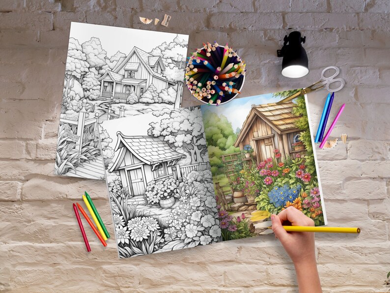 May include: An open coloring book with two pages showing black and white illustrations of houses and gardens. The left page is a finished illustration of a house and garden with colorful flowers and a blue sky. A person is coloring the right page with a yellow pencil.