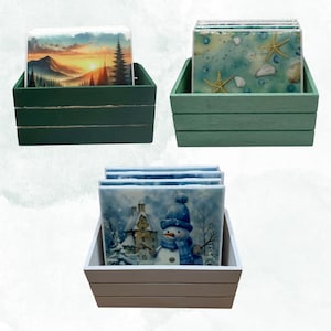 Peut inclure: Trois ensembles de dessous-de-verre dans des caisses en bois. Le premier ensemble présente une scène de coucher de soleil sur une montagne, le deuxième ensemble présente un motif de coquillages et d'étoiles de mer, et le troisième ensemble présente un bonhomme de neige dans une scène d'hiver.