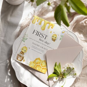 May include: A yellow and white invitation card with a bee illustration and the text "FIRST bee-day!"  Join us to celebrate the first birthday of Naomi Grace. Saturday, April 22 at 2:00 PM. 341 Anywhere St. Any City, ST 12345. RSVP by Jan 12 at 621.555.2990.