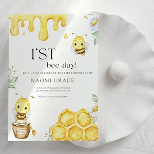 May include: A white invitation card with a yellow honeycomb design and a cartoon bee illustration. The text on the card reads "1'ST bee-day!" and "Join us to celebrate the first birthday of Naomi Grace".