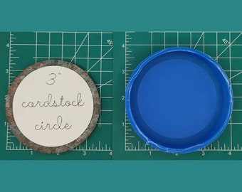 Op de afbeelding: Een cirkel met een diameter van 7,6 cm, uitgesneden uit bruin karton. De cirkel ligt op een groene snijmat. Ernaast ligt een blauwe siliconen mal van dezelfde grootte.