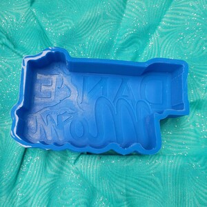 May include: Blue silicone mold for making a cake or other dessert. The mold is shaped like the words "Grandma's Famous".