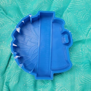 May include: Blue silicone mold shaped like a football helmet. The mold has a detailed design and a flat back.