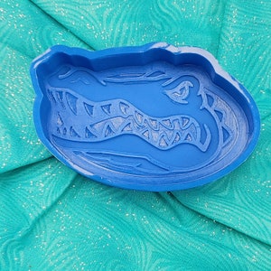 May include: Blue silicone mold shaped like an alligator head. The mold has a detailed design of the alligator's teeth and scales.