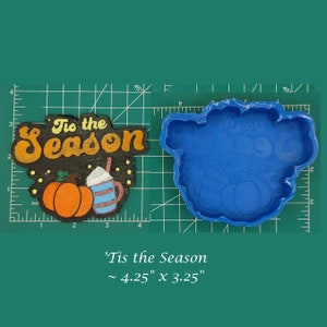 May include: A blue silicone mould for making a fall-themed cookie or cake. The mould is shaped like a pumpkin, a cup of coffee, and the words "Tis the Season". The mould is approximately 4.25 inches by 3.25 inches.