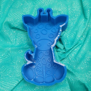 Könnte beinhalten: Ein blauer Ausstecher in Form einer Giraffe. Der Ausstecher hat ein detailliertes Design mit Flecken und Gesichtszügen. Die Giraffe sitzt aufrecht. Der Hintergrund ist ein türkisfarbener Stoff.