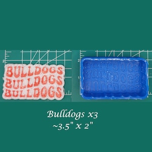 May include: A blue silicone mold for making soap or resin. The mold is shaped like a rectangle and has the word "Bulldogs" repeated three times in a wavy font. The mold measures approximately 3.5 inches by 2 inches.