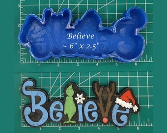 Pode incluir: Uma forma de silicone azul para assar um letreiro de "Believe" com um Grinch, uma rena e um chapéu de Papai Noel. A forma mede aproximadamente 15 cm de comprimento e 6 cm de largura.