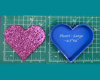 May include: A textured, pink heart shape and a blue heart-shaped mold are displayed on a green grid. The blue mold is labeled "Heart - Large ~4.5"x4". The pink heart is approximately 4.5 inches wide and 4 inches tall.
