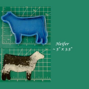 May include: Blue plastic mold of a heifer, approximately 5 inches by 3.5 inches, on a green cutting mat. A black and white heifer cutout is also shown on the mat.