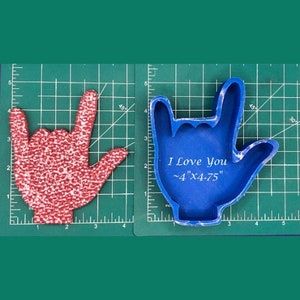 May include: Blue silicone mould of a hand making the sign for "I love you" in American Sign Language. The mould is on a green cutting mat with a ruler. The mould is approximately 4 inches by 4.75 inches.