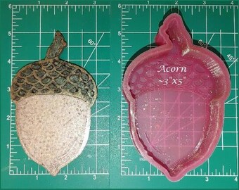 Puede incluir: Un molde de silicona rosa con forma de bellota. El molde mide 7,6 cm por 12,7 cm y tiene las palabras "Acorn ~3"x5" escritas en él.