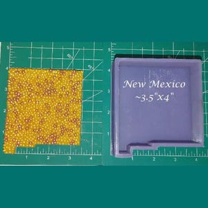 May include: A purple silicone mold shaped like the state of New Mexico. The mold is on a green cutting mat with a ruler. The mold is approximately 3.5 inches by 4 inches.