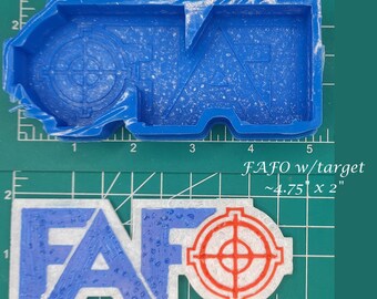 Puede incluir: Molde de silicona azul y producto terminado. El molde tiene la forma de las letras FAFO con un símbolo de diana. El producto terminado es blanco con letras azules y una diana roja. El producto terminado mide aproximadamente 12,07 cm x 5,08 cm.