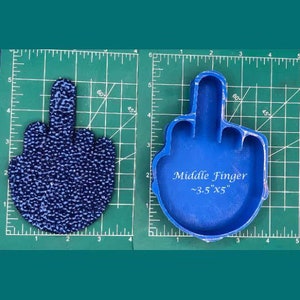May include: Blue silicone mold of a middle finger, approximately 3.5 inches by 5 inches. The mold is on a green grid background.