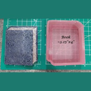 May include: A pink silicone mold for making a book-shaped soap or candle. The mold is approximately 3.25 inches by 4 inches.