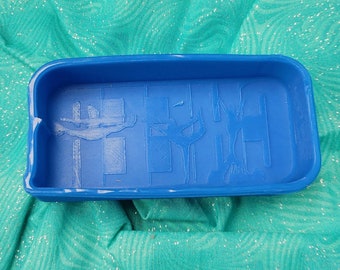 Puede incluir: Un molde de silicona azul con un diseño en relieve de dos figuras haciendo gimnasia en una barra. El molde es rectangular y tiene una superficie lisa.