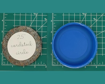 Op de afbeelding: Een 2,5 inch kartonnen cirkel, getoond naast een blauwe plastic cirkelvorm. De kartonnen cirkel is bruin en heeft een getextureerd oppervlak.