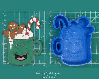 May include: A blue silicone mold for making a gingerbread man hot cocoa mug. The mold is 3.75 inches by 4.5 inches and shows a green mug with a smiling face, a candy cane, and a gingerbread man on top of the cocoa.