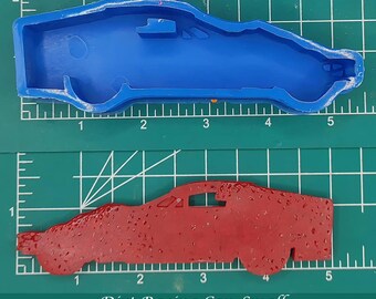 May include: A blue silicone mold of a small dirt racing car, and a red resin casting of the same car. The mold and casting are both approximately 5 inches long and 1.5 inches wide. The text "Dirt Racing Car, Small ~ 5" x 1.5" " is printed below the image.