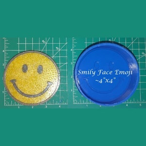 May include: A yellow smiley face emoji silicone mold, 4 inches by 4 inches, on a green grid background. The mold is blue and has the text "Smily Face Emoji ~4"x4" written on it.