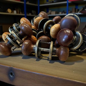 May include: A collection of wooden door knobs in various shades of brown, with brass or metal hardware. The knobs have a rounded or oval shape, and some show visible wood grain. The hardware includes plates and spindles.