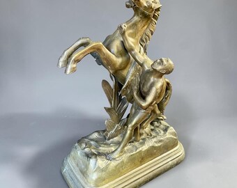 Puede incluir: Escultura de bronce que representa un caballo encabritado y una figura. La escultura tiene una base detallada y presenta un diseño clásico. El caballo está en el aire, y la figura parece estar agarrada al caballo. La escultura tiene un acabado de bronce.