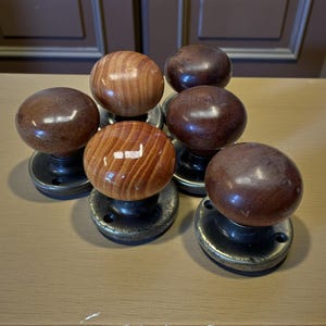 May include: Seven wooden door knobs with a polished finish. Some are stained dark brown, others show natural wood grain. Each round knob is mounted on a circular, dark metal base. Ideal for interior doors.