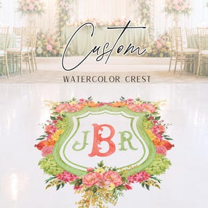 May include: A custom watercolor crest design featuring the initials "JBR" in coral and green, surrounded by a floral arrangement of pink, yellow, and green flowers. The crest is set against a blurred background of a wedding reception.
