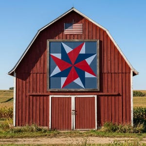 Könnte beinhalten: Eine rote Scheune mit einem großen Stern-Quiltblock in Rot-, Weiß- und Blautönen. Eine amerikanische Flagge hängt über dem Quiltblock. Die Scheunentore sind geschlossen und der Himmel ist klar blau.