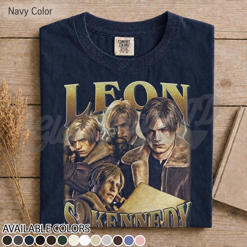 May include: A navy blue t-shirt featuring a graphic print of the character Leon Kennedy from Resident Evil. The design includes multiple depictions of the character in a brown jacket, with the name LEON KENNEDY printed in large gold letters.