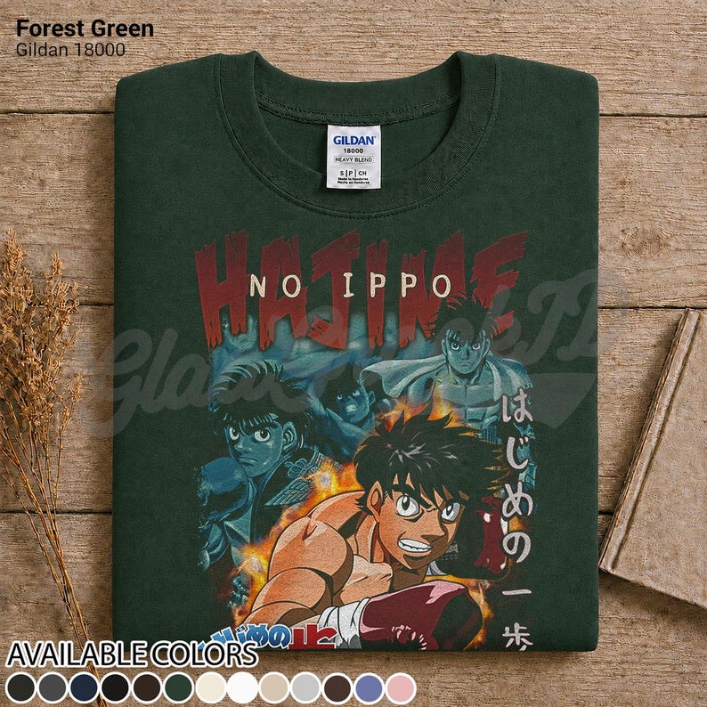 Op de afbeelding: Een bosgroen t-shirt met ronde hals en een grafische print van de anime Hajime no Ippo. Het ontwerp toont meerdere personages in bokshoudingen met vlammen en de tekst Hajime No Ippo in rood en wit. Een Gildan 18000 label is zichtbaar.