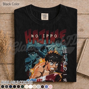 Op de afbeelding: Een zwart t-shirt met korte mouwen en een grafische print van de anime Hajime no Ippo. Het ontwerp toont meerdere personages in bokshoudingen met vlammen, de tekst HAJIME NO IPPO in het rood en Japanse tekens aan de rechterkant.