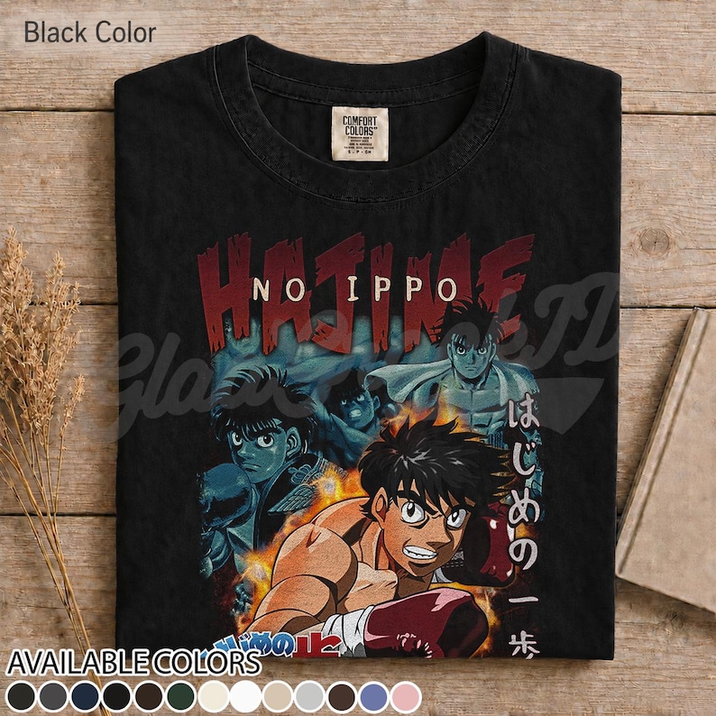 Op de afbeelding: Een zwart t-shirt met korte mouwen en een grafische print van de anime Hajime no Ippo. Het ontwerp toont meerdere personages in bokshoudingen met vlammen, de tekst HAJIME NO IPPO in het rood en Japanse tekens aan de rechterkant.