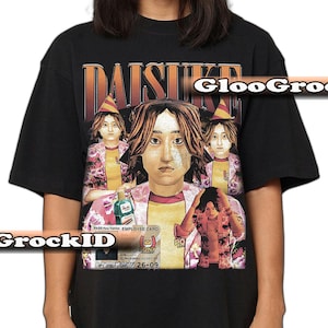 Peut inclure: T-shirt noir avec un graphisme représentant une personne et plusieurs images d'elle-même, avec le mot "DAISUKE" au-dessus. Le t-shirt comporte également un graphisme de carte d'employé et le texte "GrockID".
