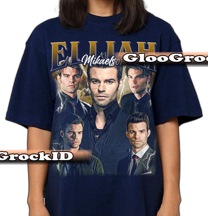 May include: Navy blue t-shirt with a collage of images of a person and the text "Elijah Mikaelson" in gold. The design includes lightning bolt graphics. A vintage-style graphic tee.