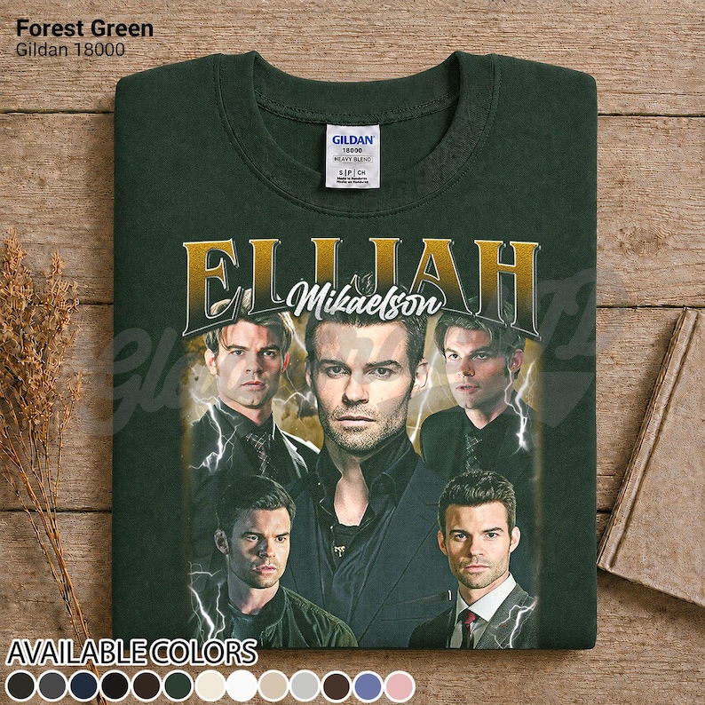 May include: Forest green Gildan 18000 sweatshirt with a gold graphic of "Elijah Mikaelson" and multiple images of a man. The sweatshirt is displayed on a wooden surface. Available in various colours.