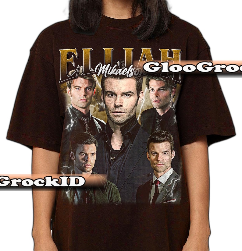 May include: A brown t-shirt with a design featuring multiple images of a man, with the name "Elijah Mikaelson" in gold. The design incorporates lightning bolt graphics and several portraits of the same person.