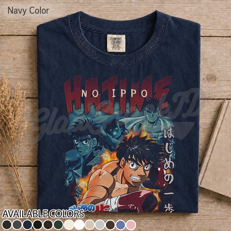 Op de afbeelding: Een marineblauw t-shirt met een grafische print van de anime Hajime no Ippo. Het ontwerp toont meerdere personages in bokshoudingen met vlammen, de tekst "HAJIME NO IPPO" in het rood en Japanse karakters verticaal aan de rechterkant.